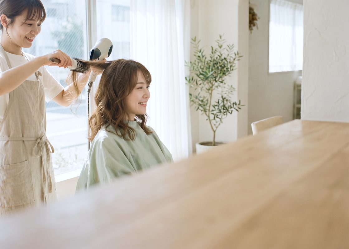 明るいヘアサロンで、スタイリストに髪を仕上げてもらい笑顔を見せる客